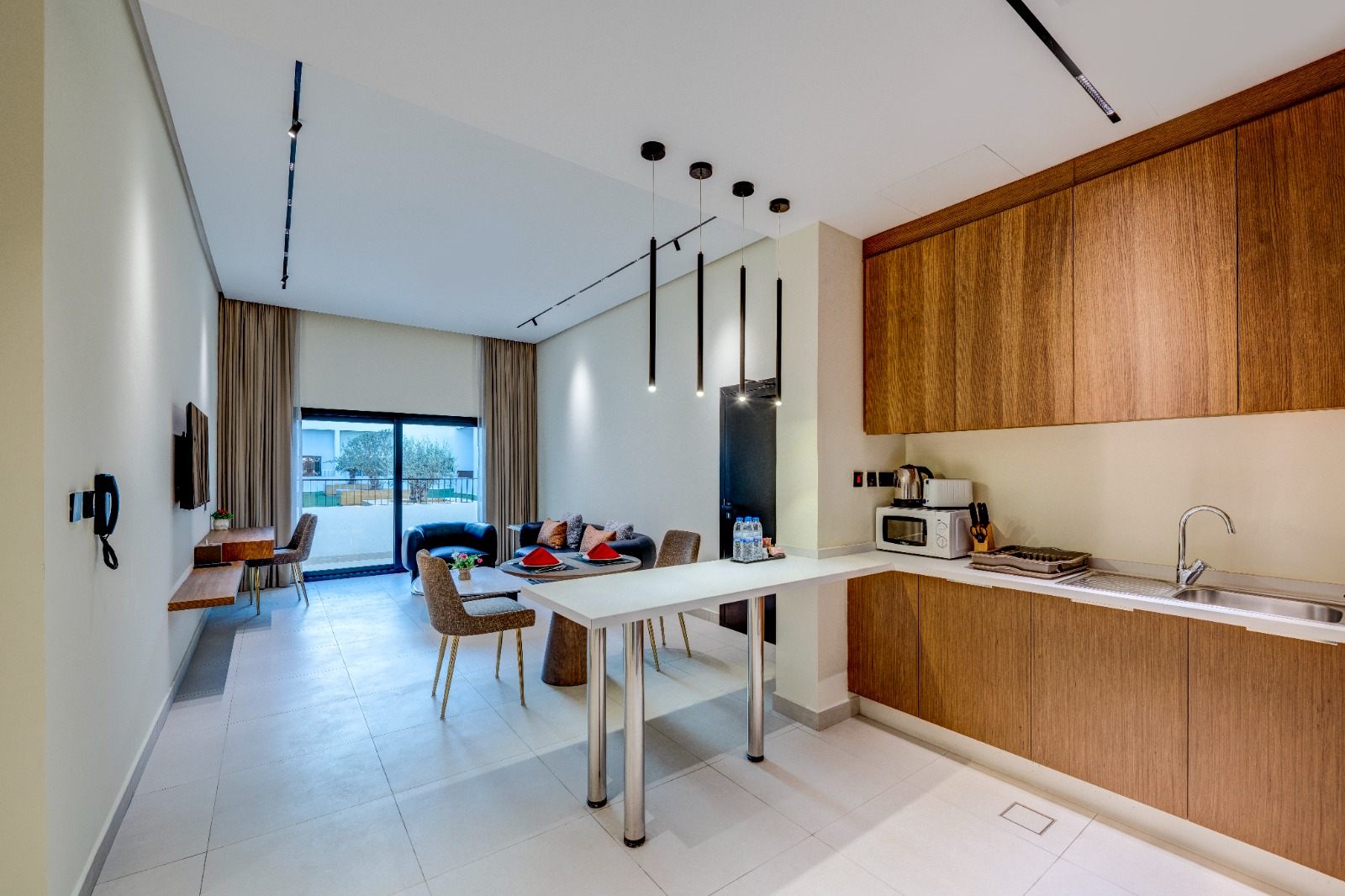 Open-plan living room and kitchen finished in warm neutral tones with balcony daylight